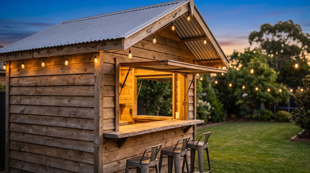 Wooden backyard bar shed with an open serving hatch, stools and string lights at dusk