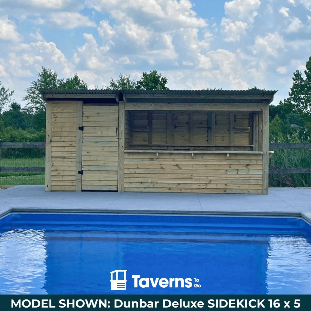 Wooden poolside cabin with a blue pool in the foreground, set against a clear sky.