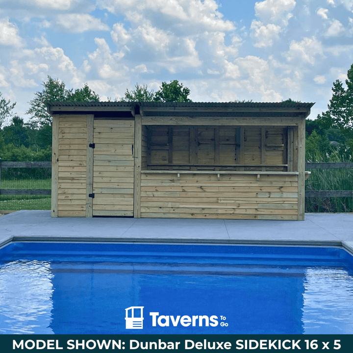 Wooden poolside cabin with a blue pool in the foreground, set against a clear sky.