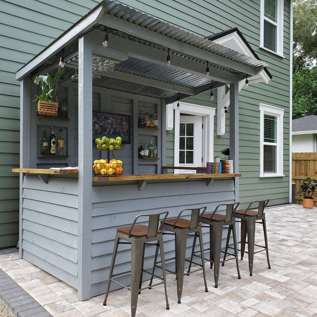 Outdoor patio area with a bar setup on a green house exterior.