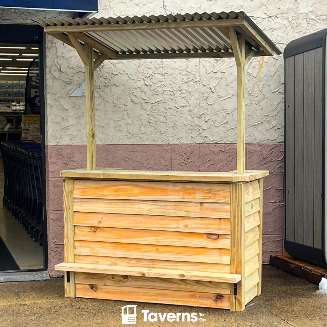 A wooden structure resembling a bar or booth with a corrugated metal roof, presumably intended for outdoor use. It is situated in front of a store, possibly for sale or display.
