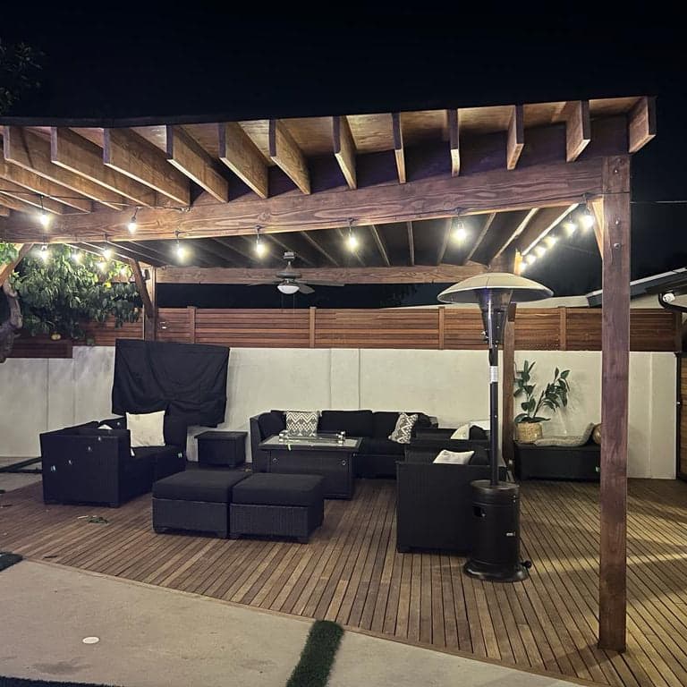 Outdoor patio area with black furniture, a wooden pergola, and string lights.