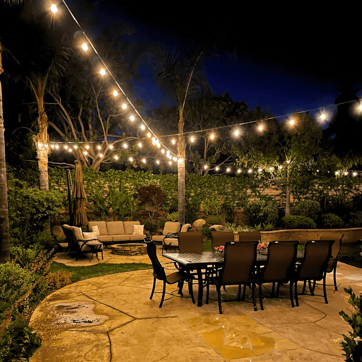 Outdoor patio with string lights, furniture, and a pool area at night.