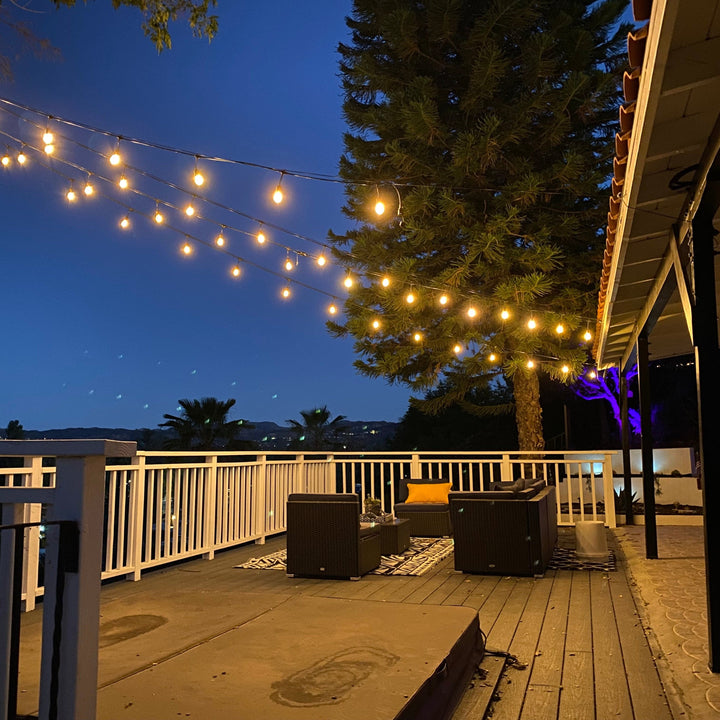 Outdoor deck with string lights, furniture, and a view of trees and mountains at night.