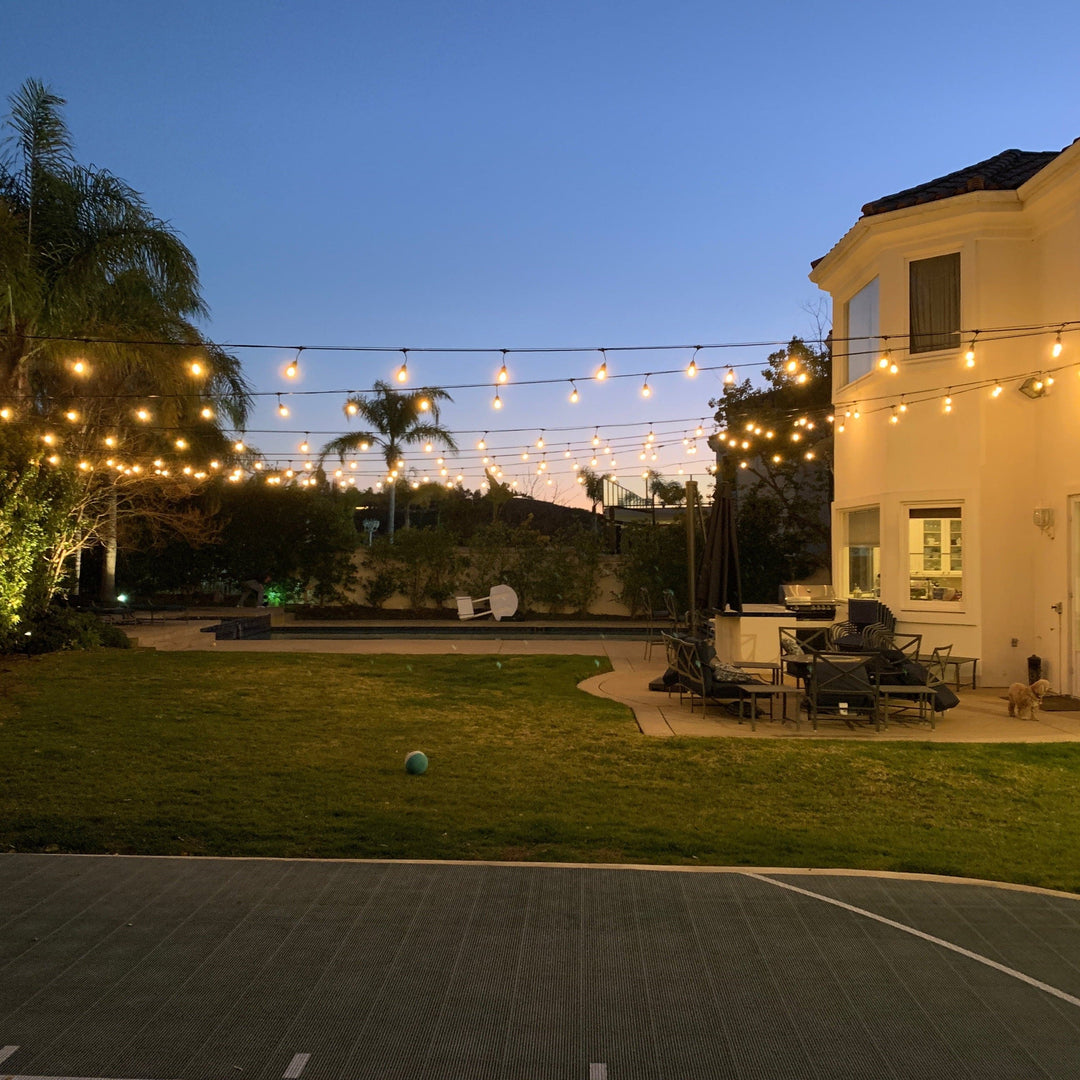 Backyard with string lights, outdoor furniture, and a tennis court at dusk.