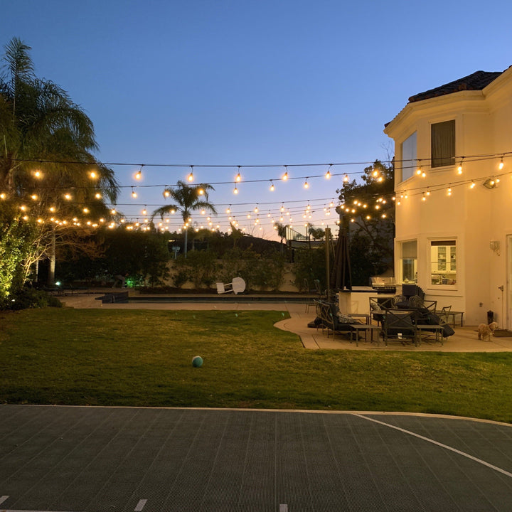 Backyard with string lights, outdoor furniture, and a tennis court at dusk.