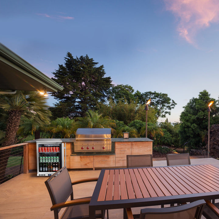 Outdoor patio setup with grill, refrigerator, and table in a garden setting