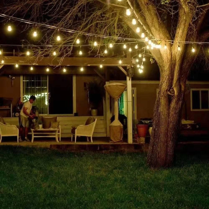 Backyard evening scene with string lights, outdoor furniture, and a tree.