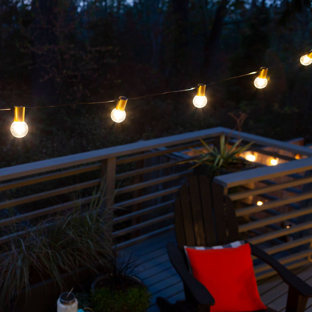 String lights on a deck with a chair and red pillow at night